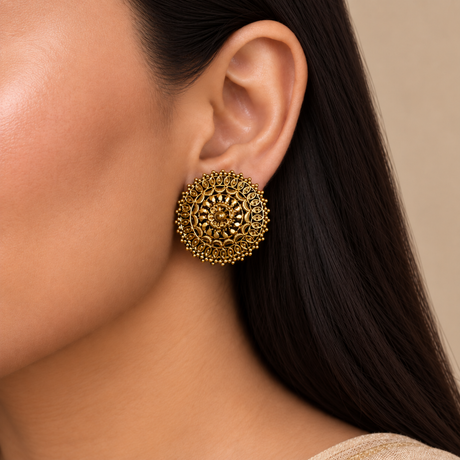 A close-up of a woman's ear wearing a large, ornate round gold earring with intricate filigree detailing.