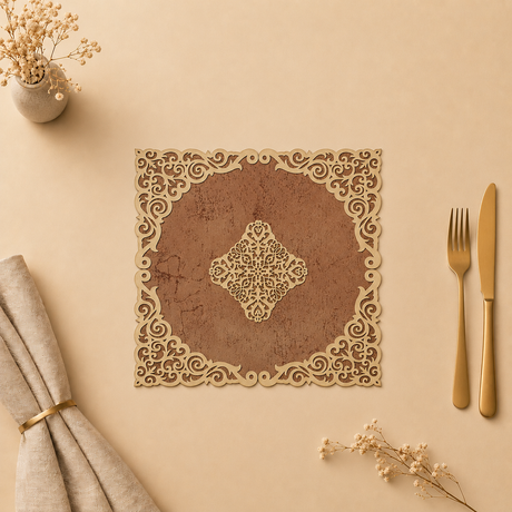 Decorative laser-cut paper placemat with gold cut-out design on a beige surface with cutlery and flowers.