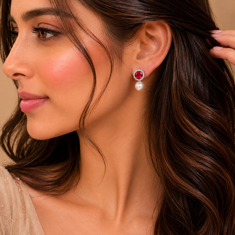 Close-up of a woman wearing a red gemstone earring with a pearl accent.