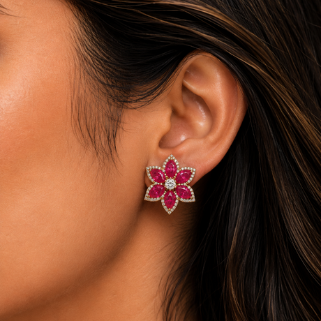 Close-up of a woman's ear wearing a floral earring with pink and green gemstones.