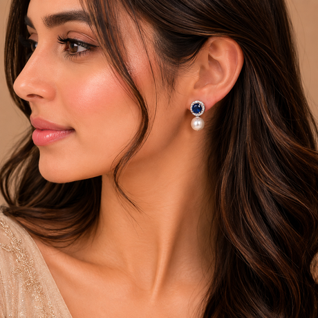Close-up of a woman wearing a pair of earrings with a blue gemstone and pearl.