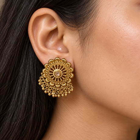 A close-up of a woman's ear wearing a large, ornate gold-toned Indian-style Kundan earring with intricate filigree and dangling beadwork.