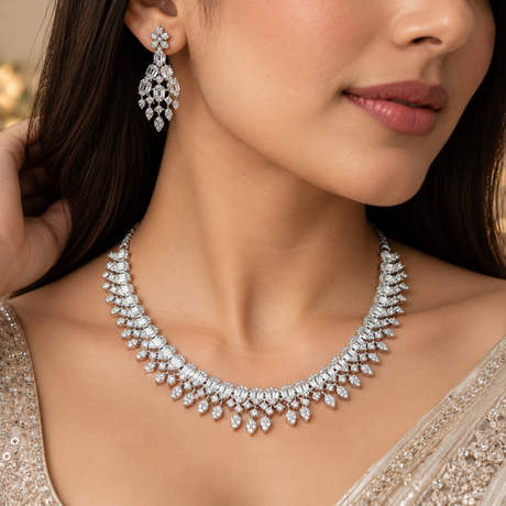 A close-up lifestyle shot of a model wearing a sparkling silver-toned diamond necklace and matching drop earrings, styled with a beige embellished gown.