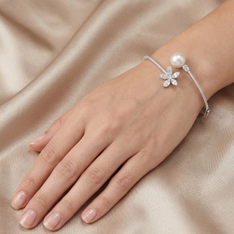 Silver bracelet with a pearl and floral design on a hand against a beige fabric background