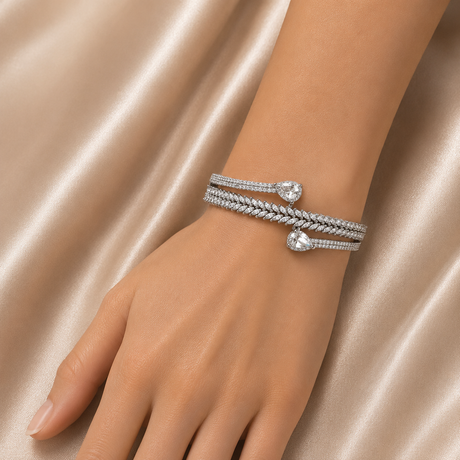 Silver bracelet with heart-shaped charms on a hand against a satin background