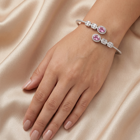 Silver bracelet with pink gemstones on a hand against a beige fabric background