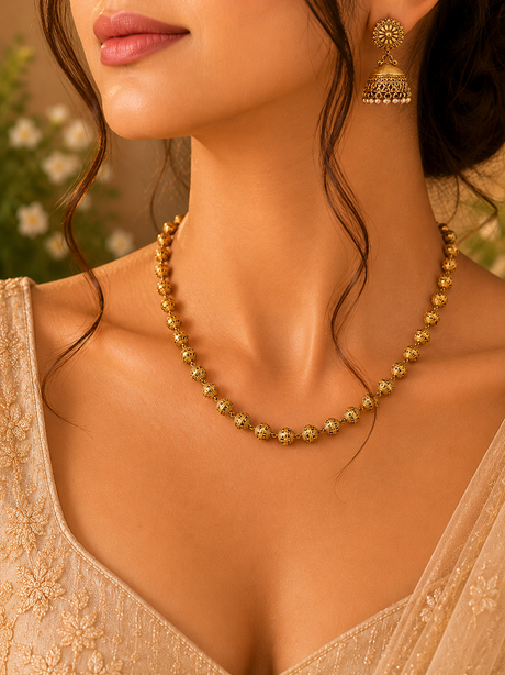 Close-up of a woman wearing a gold necklace and earrings with a blurred floral background
