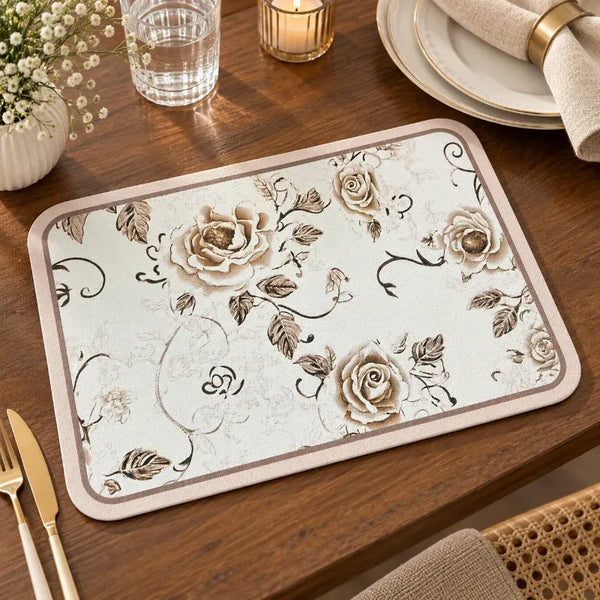 A rectangular table mat with a beige and brown rose pattern, displayed on a wooden dining table alongside a gold knife, glass, and plates.