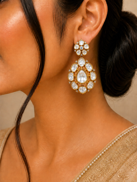 Close-up of a woman wearing a gold and crystal earring with a neutral background