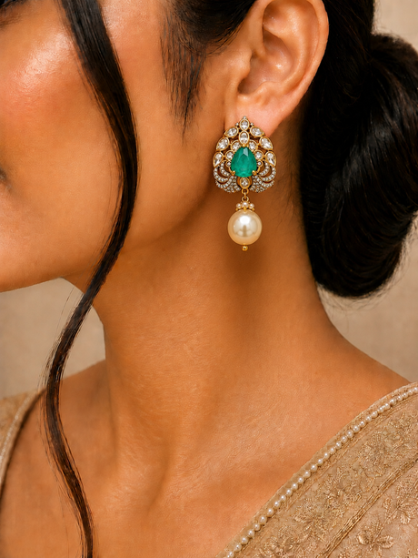 Close-up of a person wearing an ornate earring with a green gemstone and pearl.