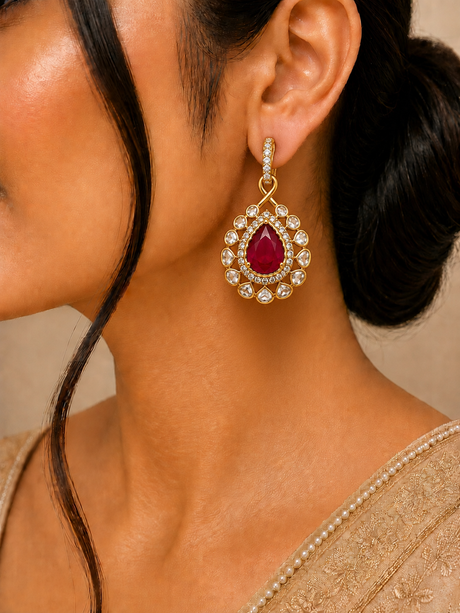 Close-up of a woman wearing a gold earring with a red gemstone on a neutral background