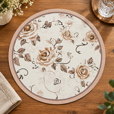 A round beige placemat with a brown floral rose pattern, displayed on a wooden table next to a folded beige napkin, small flowers, and a glass of water.