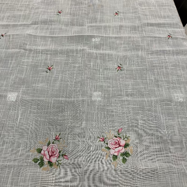 A light beige woven table runner with a subtle grid texture, decorated with pink rose motifs and small green and red floral accents.
