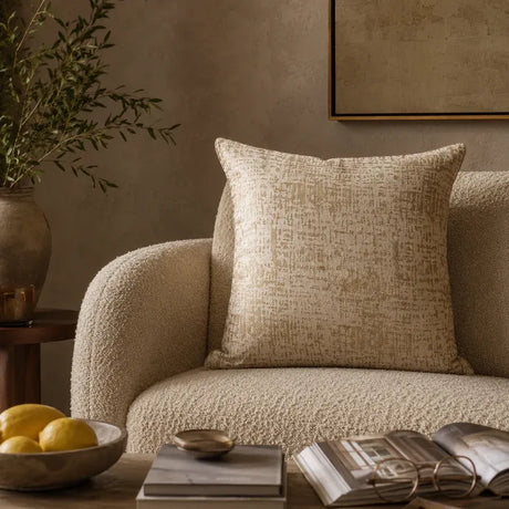Beige and gold cushion cover on a cream boucle sofa in a neutral living room