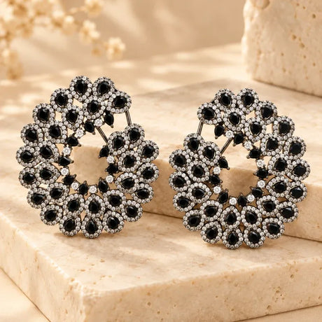 Pair of Noctelle black stone Victorian AD earrings displayed on beige marble with sparkling clear CZ accents